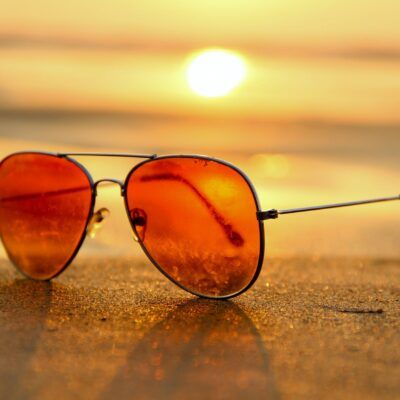 red lens sunglasses on sand near sea at sunset selective focus photography